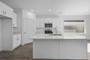 Kitchen featuring stainless steel appliances, an island with sink, dark wood finished floors, white cabinets, and recessed lighting