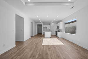Kitchen featuring open floor plan, white cabinets, a kitchen island with sink, light wood-style flooring, and stainless steel appliances