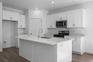 Kitchen featuring stainless steel appliances, white cabinetry, a kitchen island with sink, dark wood-style floors, and light stone countertops