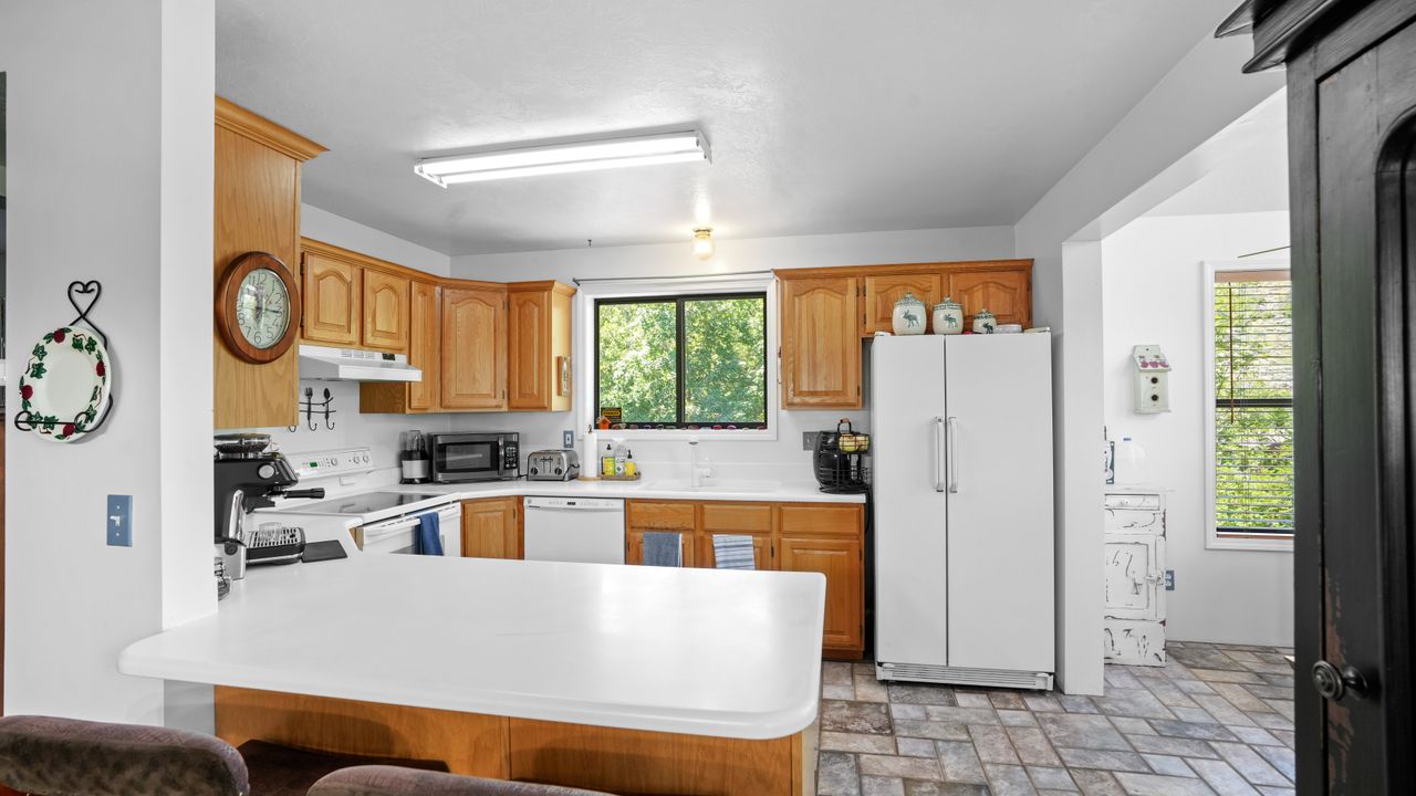 Kitchen with light countertops, white appliances, a peninsula, and wood finish cabinets