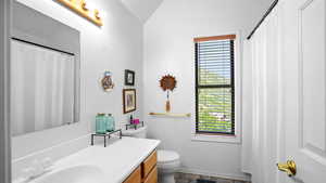 Full bathroom featuring vanity, a shower with shower curtain, dark stone finish floors, and lofted ceiling