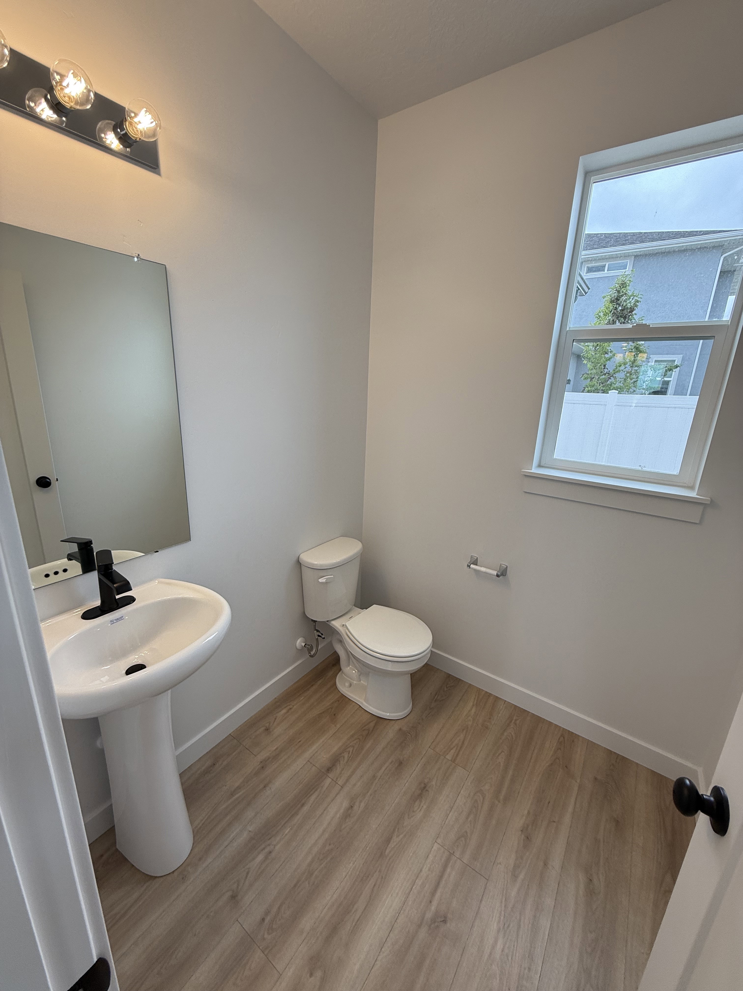 Pedestal sink with a matte black faucet, wall-mounted mirror, and vanity lighting