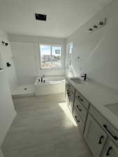 Full bath with double vanity, a bath, a textured ceiling, and walk in shower