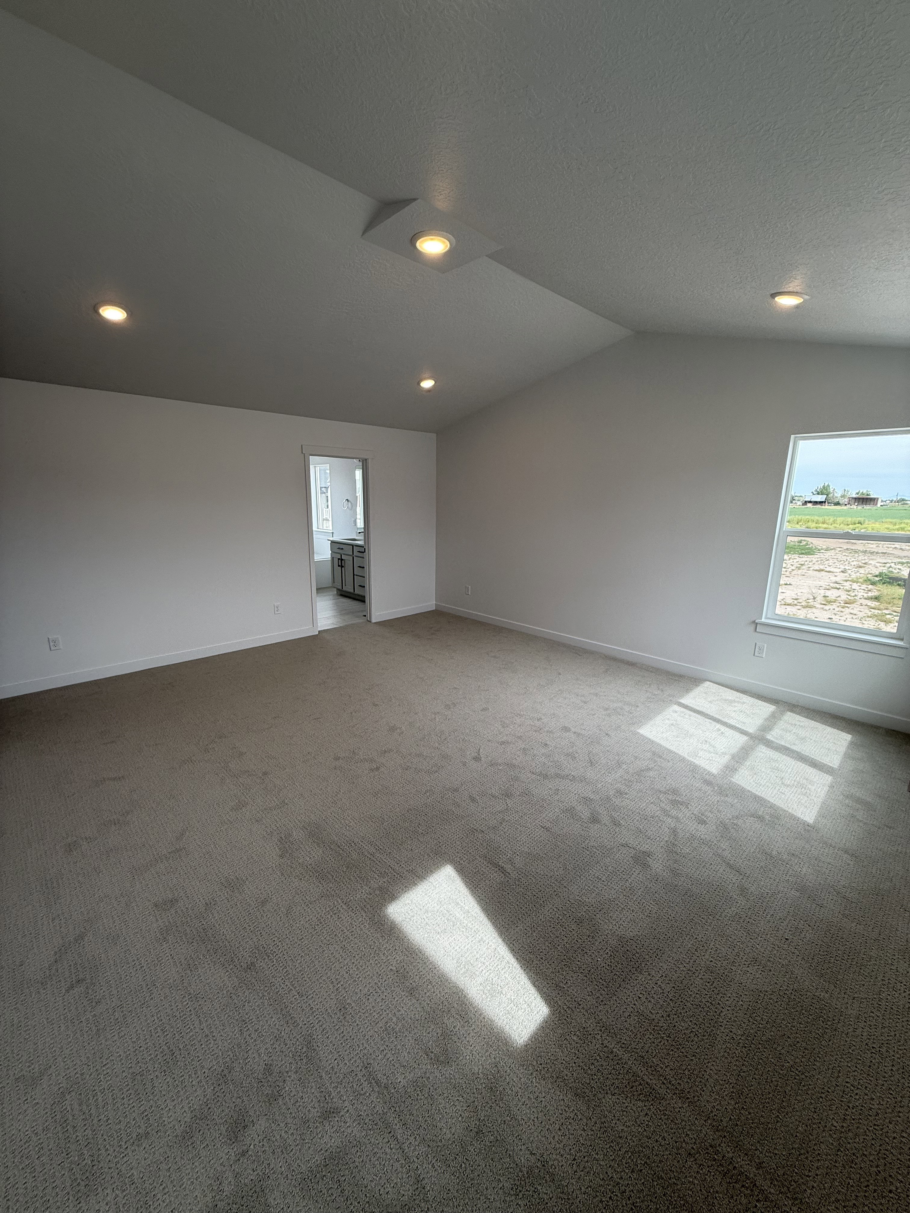 Spacious primary bedroom featuring vaulted ceilings, recessed lighting, neutral carpet flooring, and a large window