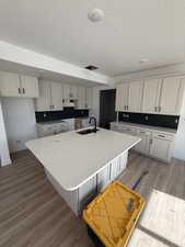 Kitchen with wood finished floors, an island with sink, a textured ceiling, light stone counters, and white cabinetry