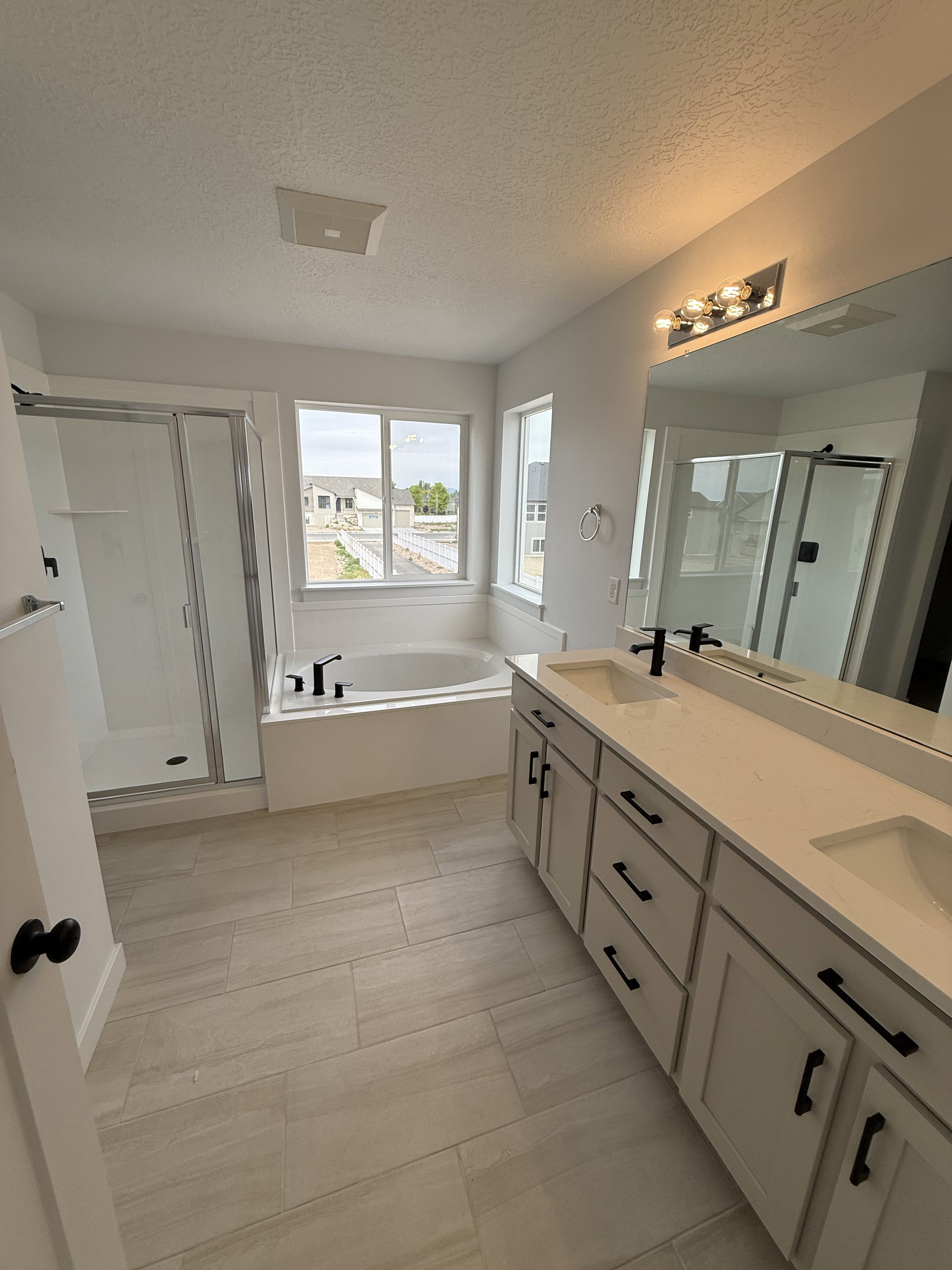 Spacious bathroom featuring a double vanity with light-toned cabinetry and countertops, a built-in soaking tub, and a separate glass-enclosed shower
