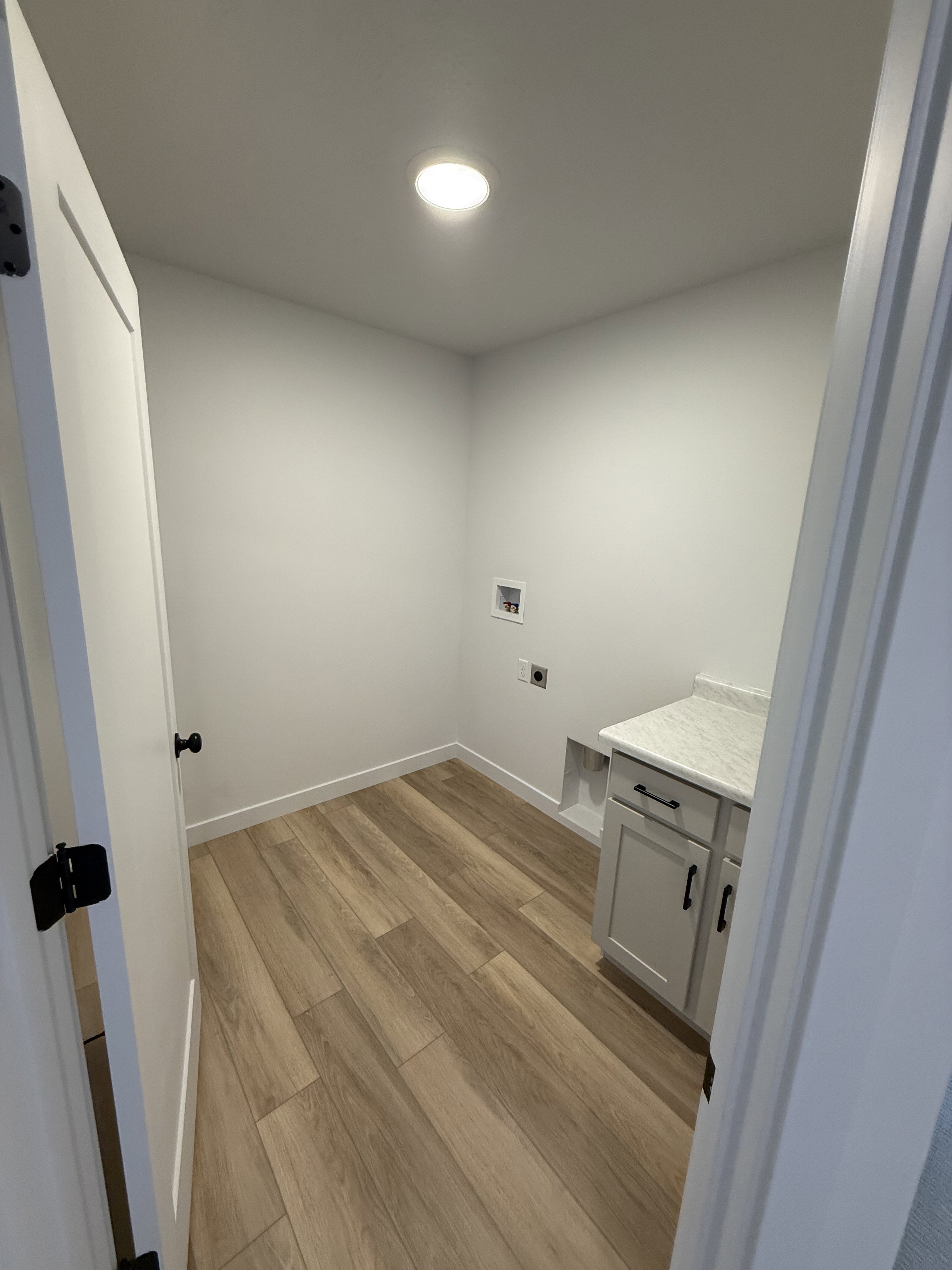 Laundry area featuring wood-finish flooring, light gray walls, built-in cabinetry with a light-colored countertop, and recessed ceiling lighting