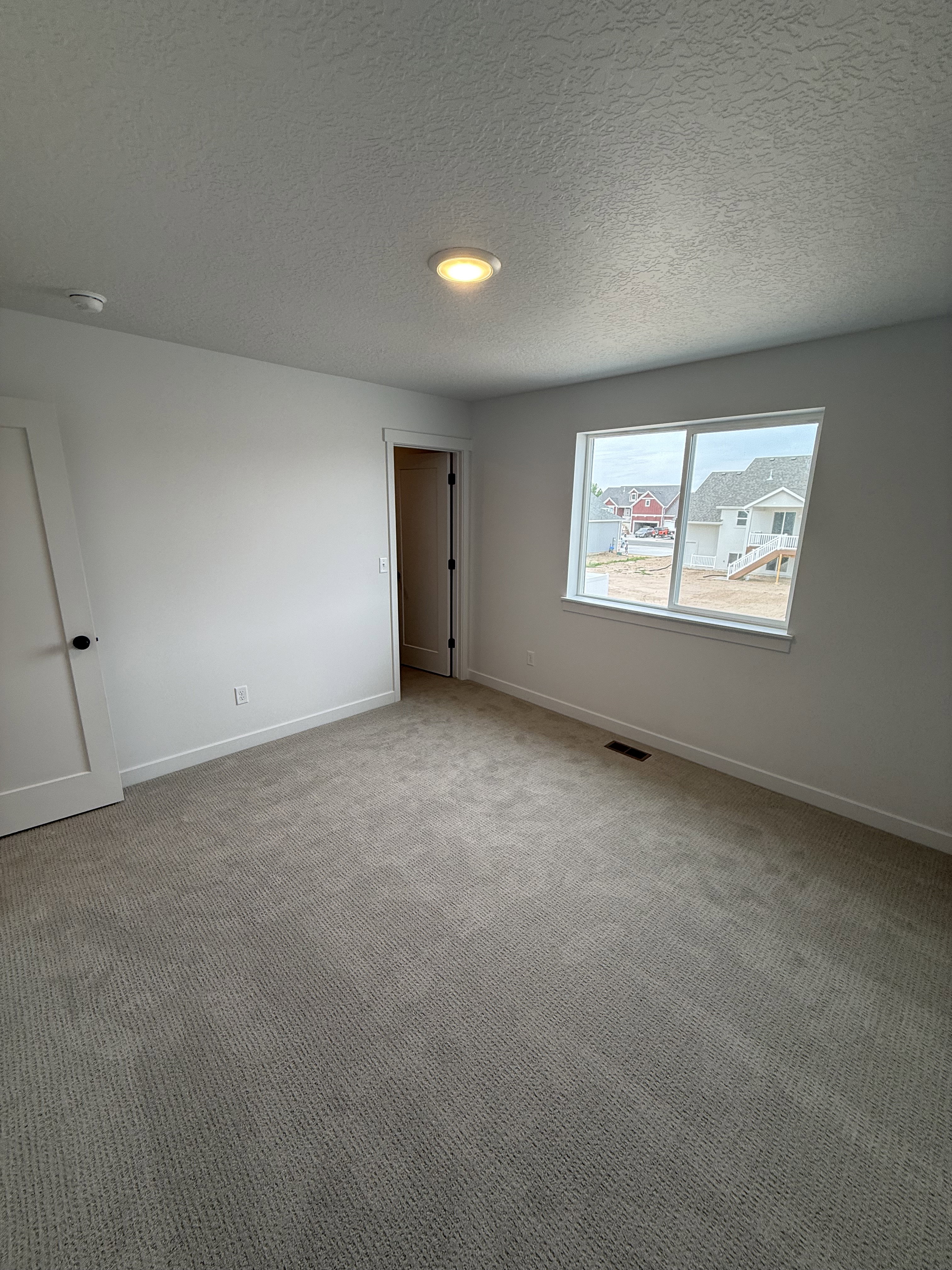 Spacious room featuring neutral carpeting, white walls, and a large window with white trim