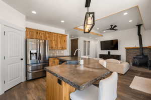 Kitchen featuring a breakfast bar area, stainless steel refrigerator with ice dispenser, a center island with sink, a wood stove, and dark wood-style floors