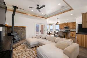 Living area with a raised ceiling, wood finished floors, a ceiling fan, a wood stove, and recessed lighting