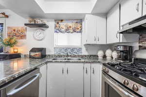 Kitchen featuring stainless steel appliances, dark countertops, and white cabinetry