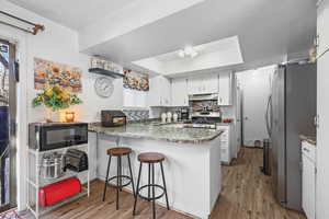 Kitchen featuring white cabinetry, a peninsula, stainless steel appliances, a kitchen bar, and dark wood-style floors
