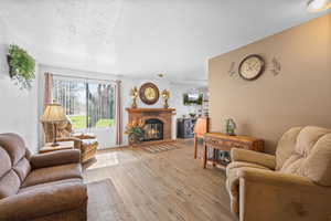 Living room featuring light wood-type flooring, a textured ceiling, and a brick fireplace