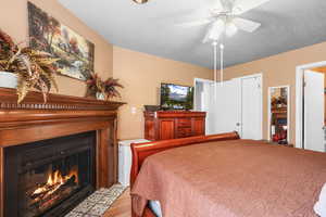 Bedroom featuring a fireplace with flush hearth, a textured ceiling, a ceiling fan, and light wood-style floors