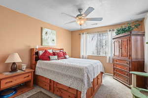 Bedroom featuring ceiling fan, a textured ceiling, and light carpet