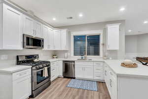 Downstairs Kitchen with stainless steel appliances, LVP flooring, a breakfast bar, white cabinetry, and recessed lighting
