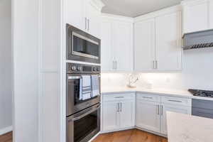 Kitchen featuring stainless steel appliances, custom cabinetry, quartz countertops, and hardwood floors
