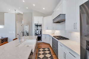 Kitchen with custom cabinetry, backsplash, quartz  counters, and stainless steel appliances