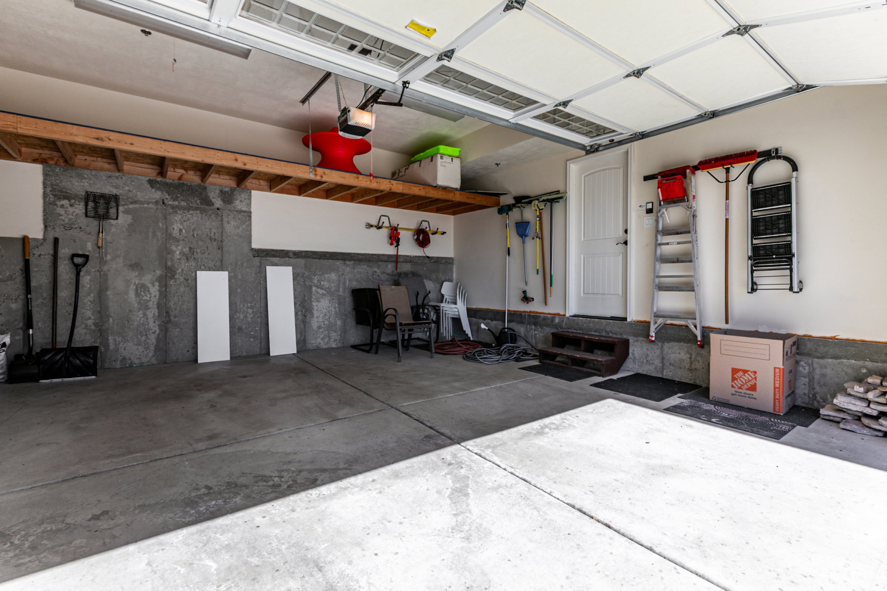 Spacious garage featuring concrete flooring, an overhead garage door, built-in overhead storage shelving, and a pedestrian door