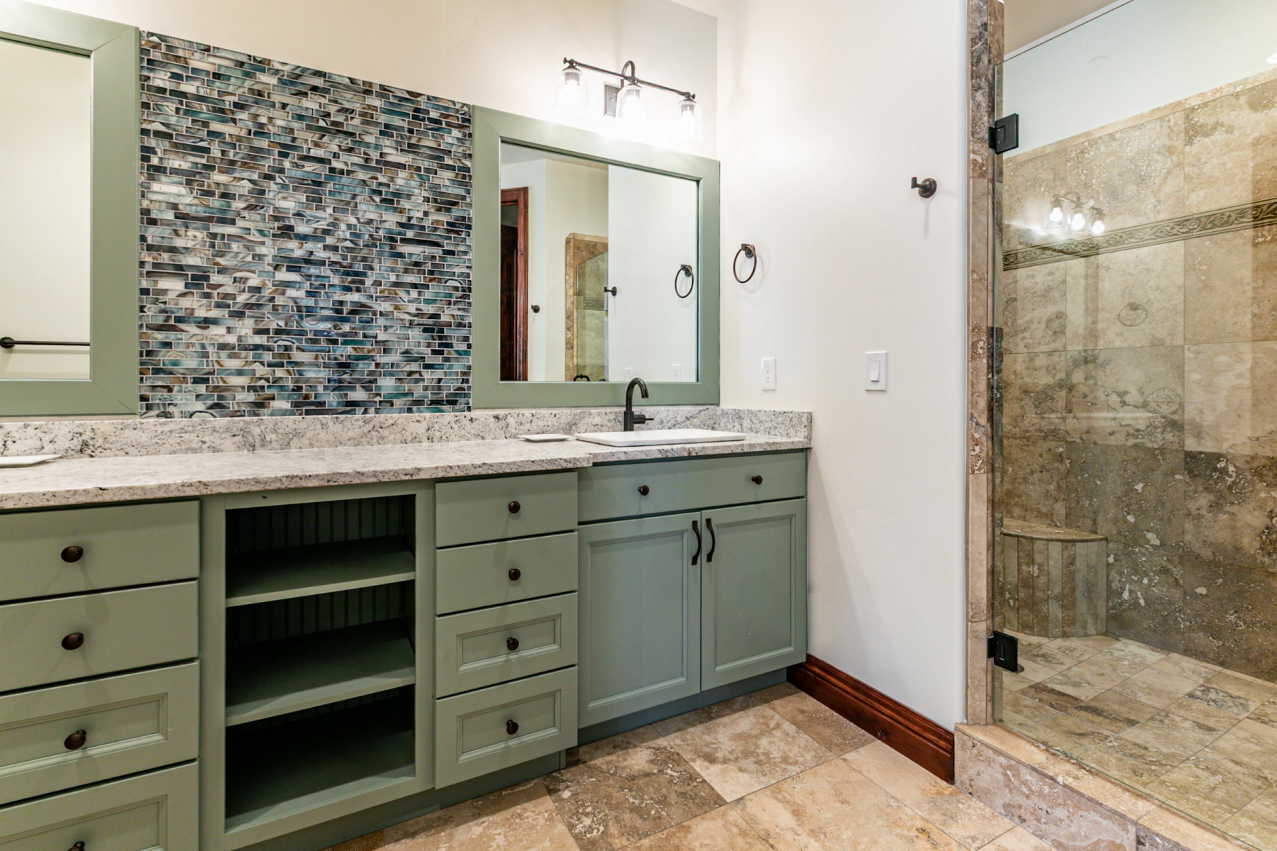 Dual vanity featuring light green cabinetry with black hardware, stone-finish countertops, and under-mount sinks