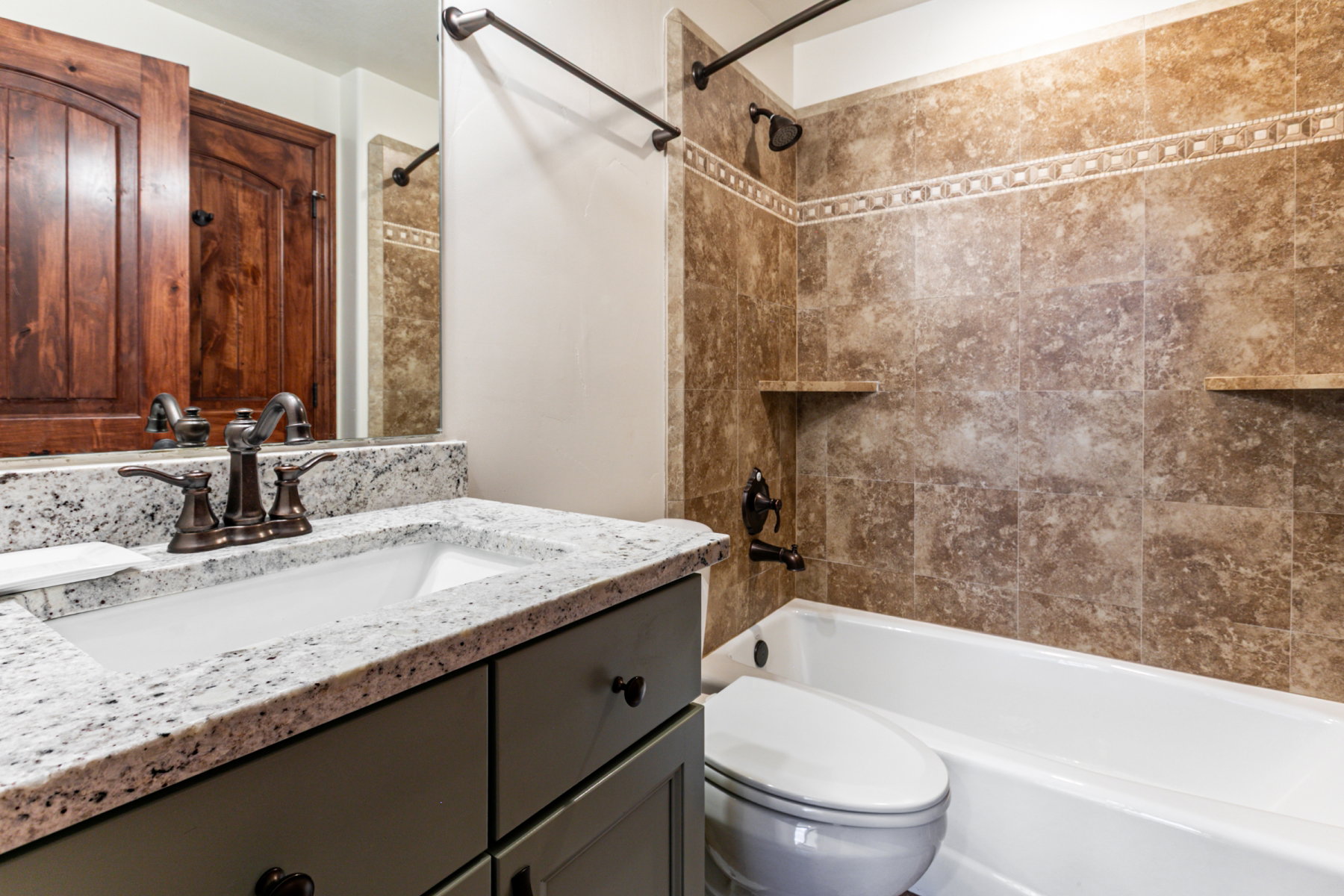 Bathroom featuring a granite countertop vanity with an undermount sink, a bronze-finish faucet, and coordinating dark cabinetry