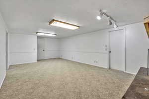 Finished below grade area with carpet flooring, a textured ceiling, and rail lighting