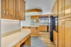 Kitchen featuring light countertops, black appliances, light wood finished floors, and wood finish cabinetry