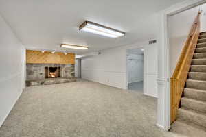 Finished below grade area with a stone fireplace, carpet, rail lighting, wooden walls, and an accent wall