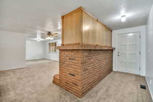 Bar featuring light colored carpet, ceiling fan, light wood finish cabinets, and a textured ceiling