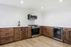 Kitchen with wine cooler, stainless steel appliances, light wood-style floors, recessed lighting, and light stone counters