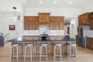 Kitchen with wood finish cabinetry, a breakfast bar, decorative backsplash, light wood-style flooring, and high quality fridge