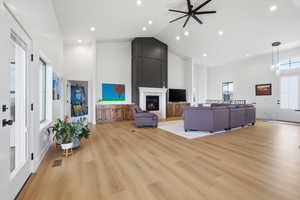 Living area with a ceiling fan, vaulted ceiling, a glass covered fireplace, light wood-style flooring, and recessed lighting