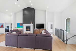 Living area with vaulted ceiling, light wood finished floors, recessed lighting, and a large fireplace