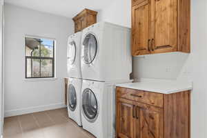 Laundry area with cabinet space, light tile patterned flooring, and stacked washer / dryer
