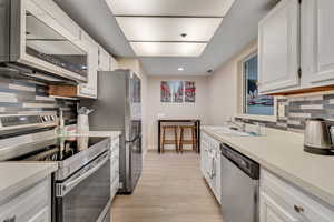 Kitchen with tasteful backsplash, stainless steel appliances, light countertops, white cabinets, and recessed lighting