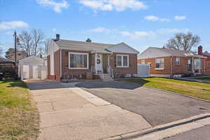 Bungalow with an outbuilding, brick siding, driveway, a chimney, and a front lawn