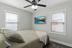 Bedroom featuring dark carpet, ceiling fan, and multiple windows