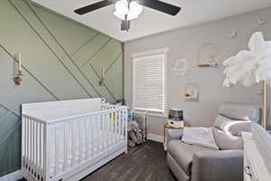 Bedroom featuring a nursery area, dark carpet, and a ceiling fan