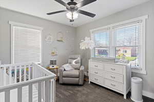 Bedroom with a nursery area, dark colored carpet, and a ceiling fan