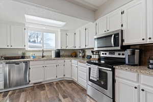 Kitchen with stainless steel appliances, white cabinetry, and light stone counters