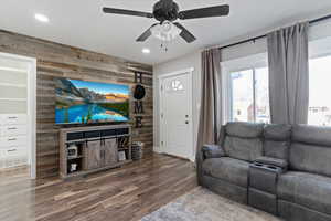 Living room featuring wood walls, recessed lighting, dark wood finished floors, a ceiling fan, and an accent wall