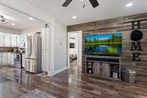 Living room featuring dark wood-style flooring, ceiling fan, wooden walls, and recessed lighting