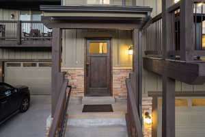 View of exterior entry featuring stone siding, a garage, board and batten siding, and driveway