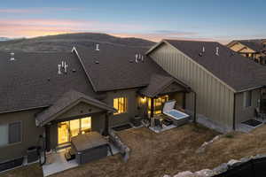 Back of property at dusk featuring a hot tub, board and batten siding, roof with shingles, and a patio