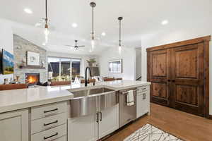 Kitchen featuring open floor plan, a ceiling fan, a stone fireplace, dark wood finished floors, and dishwasher