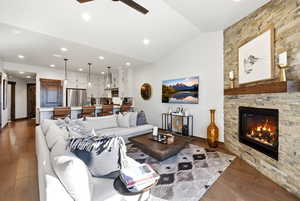 Living room featuring a ceiling fan, a stone fireplace, lofted ceiling, dark wood-style flooring, and recessed lighting
