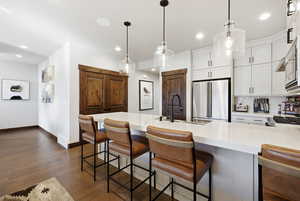 Kitchen with a kitchen bar, dark wood-style floors, high end refrigerator, a peninsula, and white cabinets
