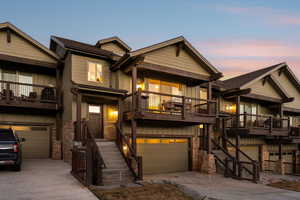 View of front of property featuring a garage, concrete driveway, board and batten siding, stone siding, and a balcony