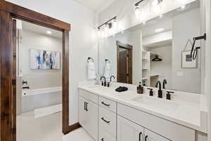Bathroom with double vanity, a tub to relax in, a spacious closet, and light tile patterned floors
