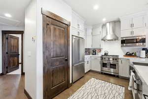 Kitchen featuring high end appliances, dark wood finished floors, decorative backsplash, white cabinetry, and recessed lighting